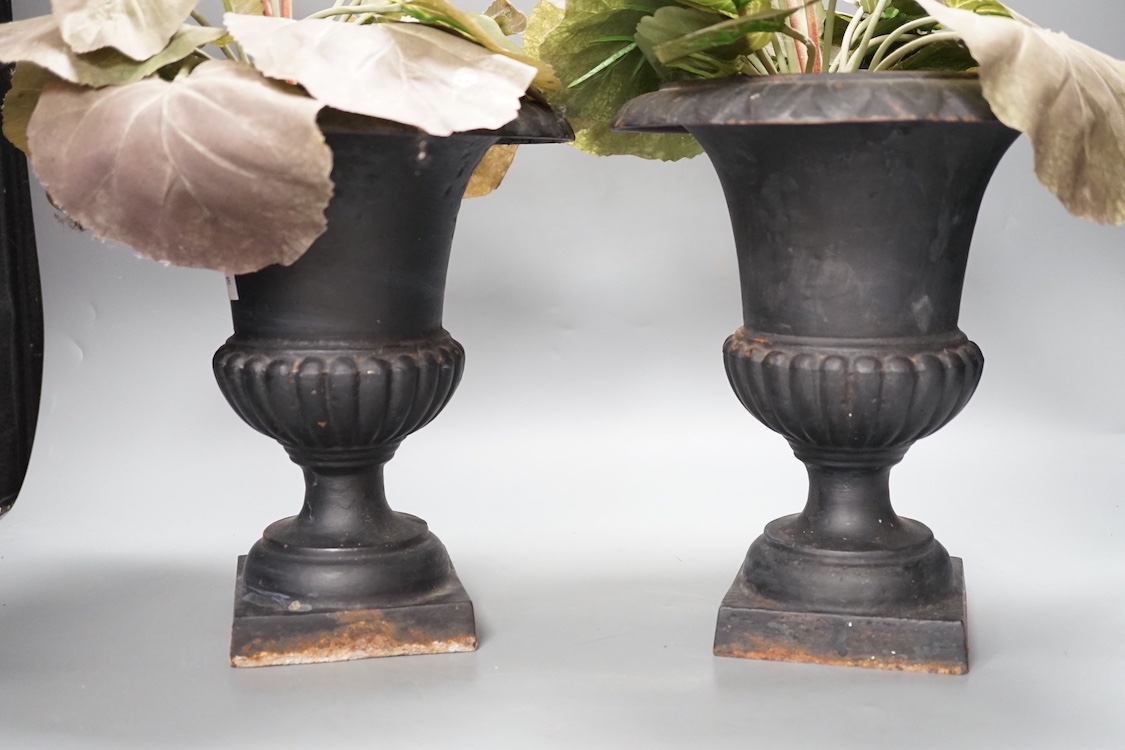 A pair of cast iron urns 25cm, containing faux plants